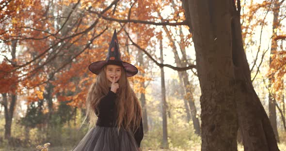 Cute Little Girl with Long Hair Looking Like a Witch in a Special Dress and Hat in the Autumn Forest