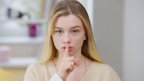 Serious Young Woman Putting Finger on Lips Showing Hush Gesture Looking at Camera