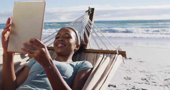 African american woman using digital tablet while lying on a hammock at the beach