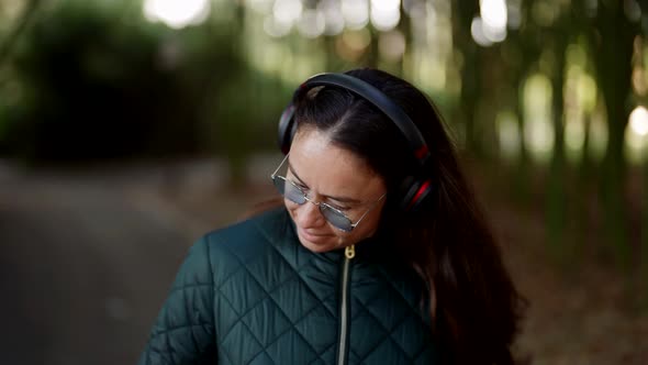 Charming Middleaged Woman is Enjoying Music By Headphones Walking in Park