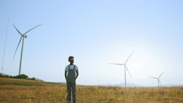 Man Standing on Field with Huge Windmills During Summer Sunset