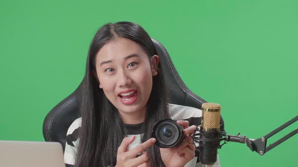 Asian Woman With Computer Reviewing Camera Len While Sitting In Front Of Green Screen