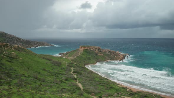 AERIAL: Flying Away From Ghajn Tuffieha Bay with Il-Qarraba Rock in Background