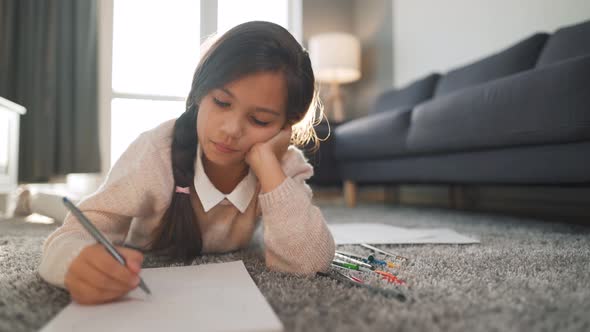 Cute Concentrated Girl Draws with Colored Pencils Lying on the Floor Alone