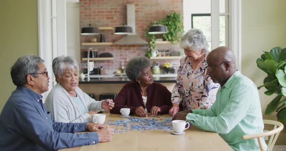 Group of happy diverse senior friends drinking coffee and doing puzzle at home