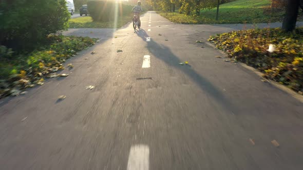 Boy rides a bicycle on bicycle path in autumm park on sunset.