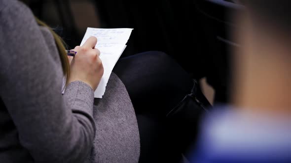 Young woman writes down information on a shirt of paper during conference.