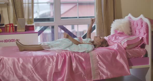 Little Caucasian Girl Lying on Pink Bed in Room, Gesturing and Talking