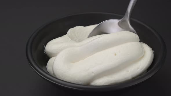 Bowl of whipped cream with spoon on black background