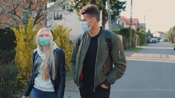 Medium Shot of Multiethnic Man and Woman in Medical Masks Walking Down the Street in Housing Estate