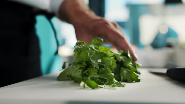 Professional kitchen of the restaurant, close-up: The chef cuts the greens herbs finely with a knife