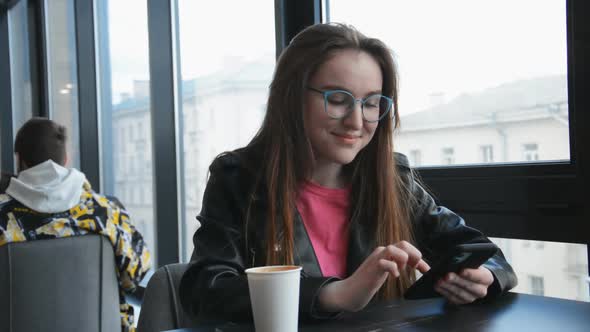 A Beautiful Young Girl with Glasses Sits in a Cafe and Writes a Message