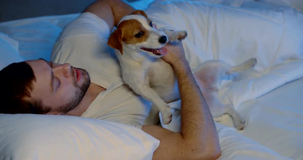 a Man Is Lying on a Sofa with White Bed Linen and Trying To Fall Asleep in an Embrace with His Dog