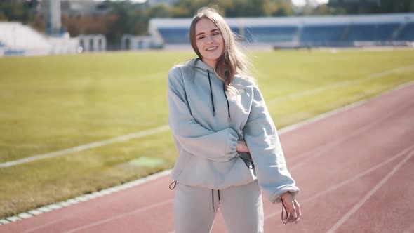 Positive Beautiful Caucasian Girl Posing at the Stadium in a Gray Tracksuit 