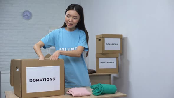 Female Volunteer Putting Clothes in Donation Box, Working in Social Center