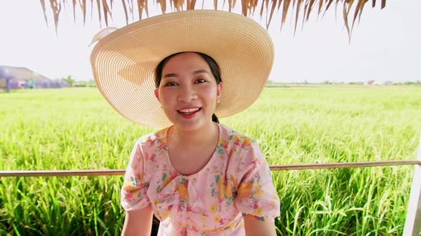 Beautiful young Asian woman with hat in rice field making video call.