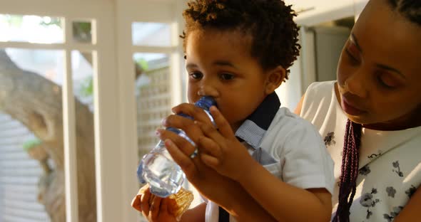 Side view of young black mother feeding water to her son in kitchen of comfortable home 4k