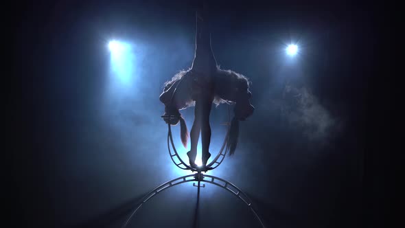 Girls Rotate in the Air While Sitting on a Hoop. Black Smoke Background. Silhouette