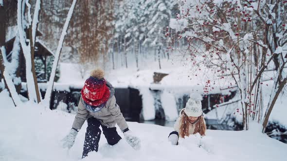 Happy children wearing warm coats and caps are throwing snow up on the snowy background.