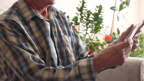 senior citizen looks at family photos while sitting in front of him on the couch at home. an elderly