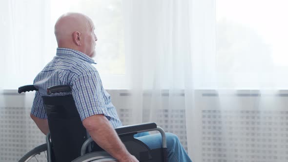 Disabled old man is sitting in a wheelchair at home alone. A handicapped person.