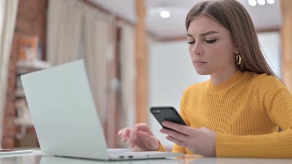 Young Woman Using Smartphone and Working on Laptop