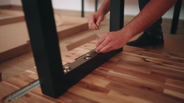 Man Mounting Metal Legs Of A Wooden Table. Fastening Screw Using Allen Key. High Angle