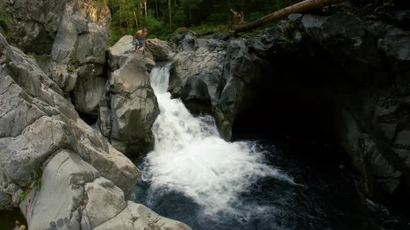 Man Cliff Diving Into Waterfall From Rocky Canyon alt