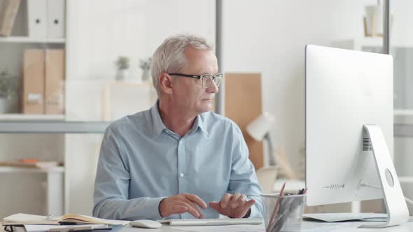 Smiling Senior Caucasian Man Working on Computer in Office