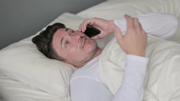 Middle Aged Man Talking on Smartphone Laying in Bed 