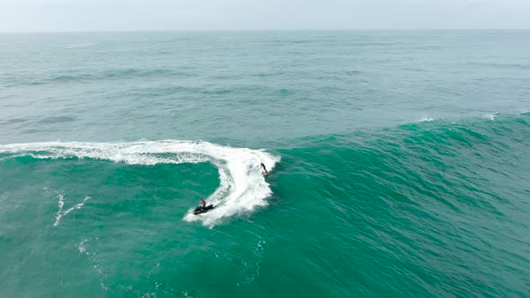 Sportsman Surfs Ocean Wave with Heavy Foam Following Scooter