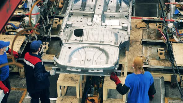 Two Car Factory Workers Moving a Car Body Using Chains