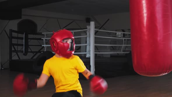 Little Boy in Protective Helmet Kicking the Punching Bag From the Turn and Hitting It with the