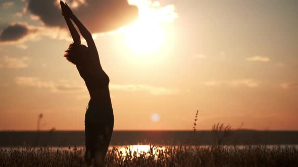 Silhouette of Young Beautiful Girl Practicing Yoga at Sunset