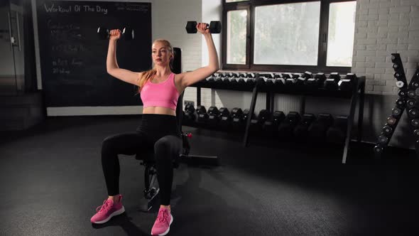 The girl does an exercise in the gym. Female athletic woman exercising shoulders with dumbbells