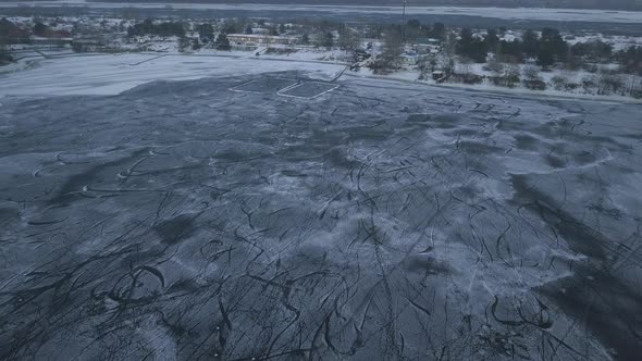 Drone Flight Over a Frozen Lake Where Children Train and Play Hockey Near the Shore on a Cloudy Day