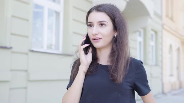 A Young Turkish Woman Talks on a Smartphone with a Smile in the Street in an Urban Area