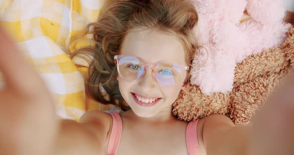 A Little Happy Girls with Glasses Rests and Sends Greetings with Her Hand