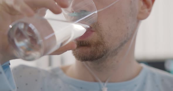 Close Up of Young Male Patient Drinking Glass of Water in Hospital