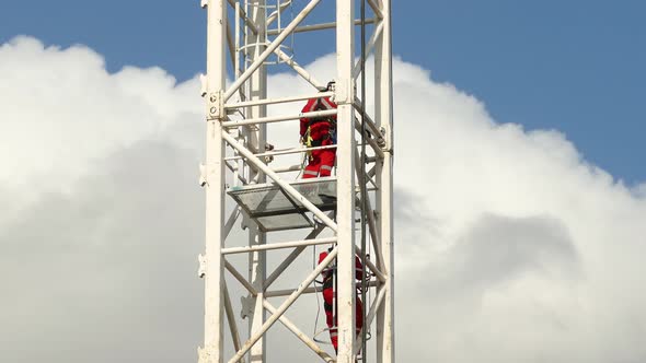 Two rescue firefighters stepping down from tall metallic electric tower.