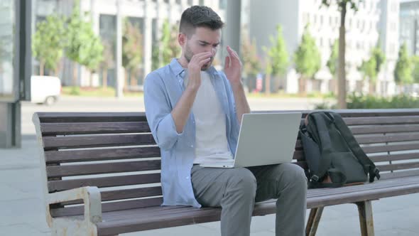 Young Man with Headache Using Laptop While Sitting on Bench