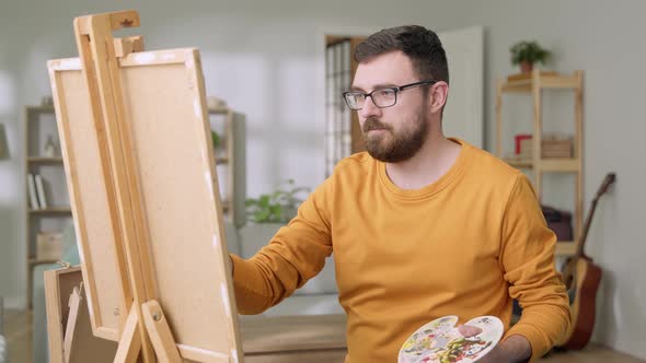 Young Man is Working in His Modern Home Studio in the Morning Drawing on Canvas Enjoying the Process