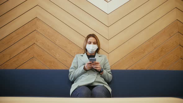Businesswoman Wearing Protective Medical Mask Sitting on the Sofa Using Phone in the Modern Office