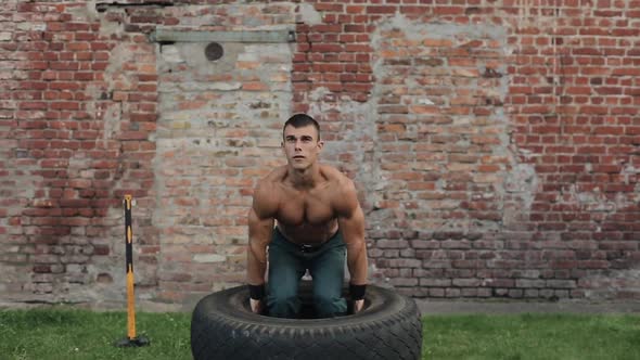 Handsome Young Man Holding a Tire and Doing Squats