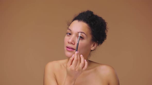 Beauty Portrait of Young African American Woman Looking in Mirror and Doing Eye Makeup Using Brush
