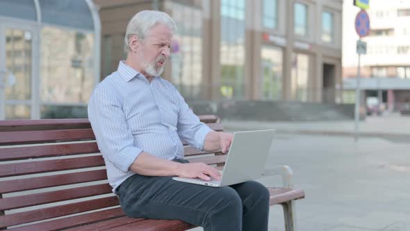 Old Man with Wrist Pain Using Laptop While Sitting on Bench