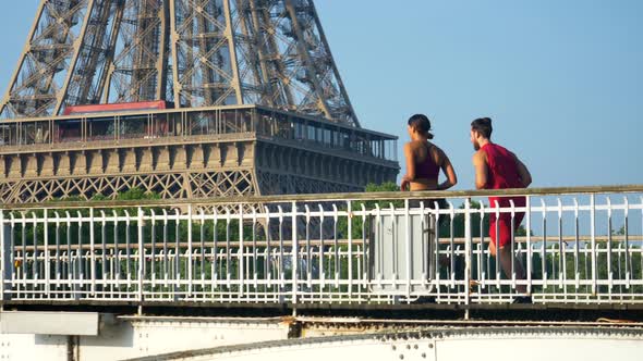 A man woman couple running across a bridge with the Eiffel Tower