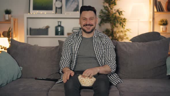 Joyful Guy Watching TV Laughing Pointing at Screen and Eating Popcorn at Home