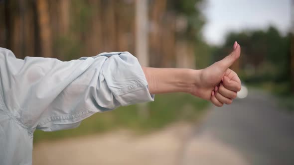 Closeup Female Hand Gesturing Thumb Up Hitchhiking with Blurred Cars Passing at Background