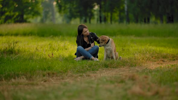 Female in Jeans and Leather Jacket Communicates with Her Outbred Dog in a Park.